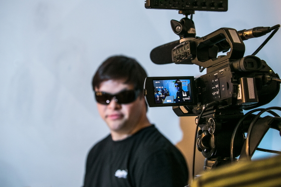 A photo of a man in black T-shirt and sunglasses being filmed