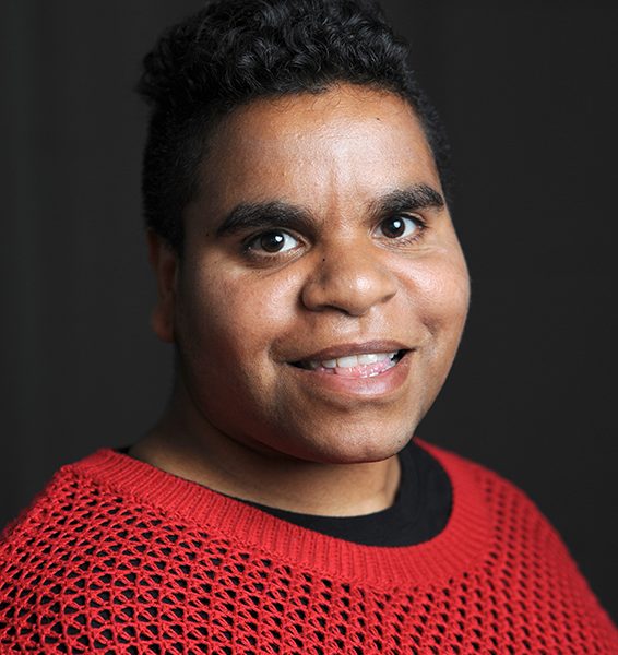 A head and shoulders portrait photo of a woman wearing a red jumper and black T-shirt