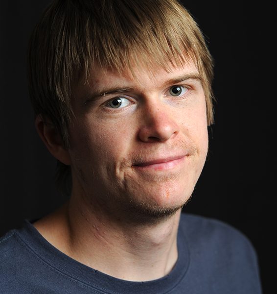 A head and shoulders portrait photo of a man wearing a grey T-shirt