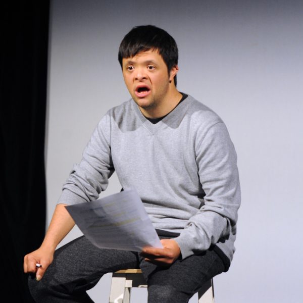 Man sitting on stool speaking from script