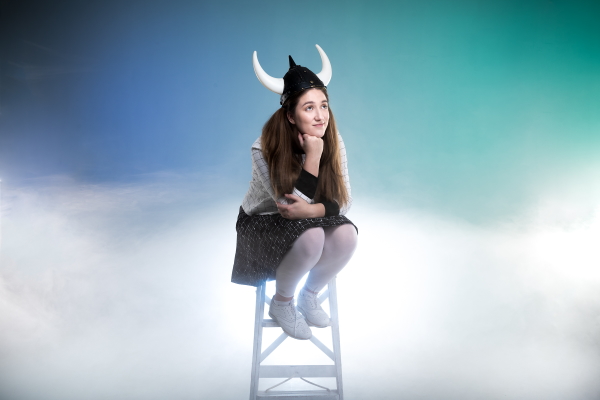A woman wearing a viking hat sitting on a stool amongst what appears to be clouds