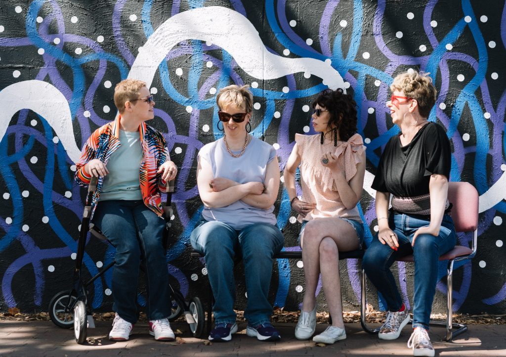 Photo of The Sisters of Invention sitting in front of an abstract mural
