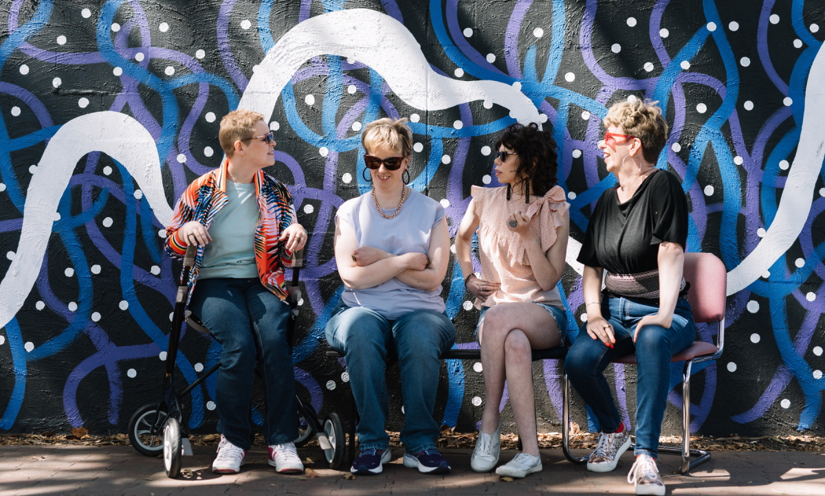 Photo of four disabled women sitting in front of an abstract mural at Tutti. One uses a powered chair