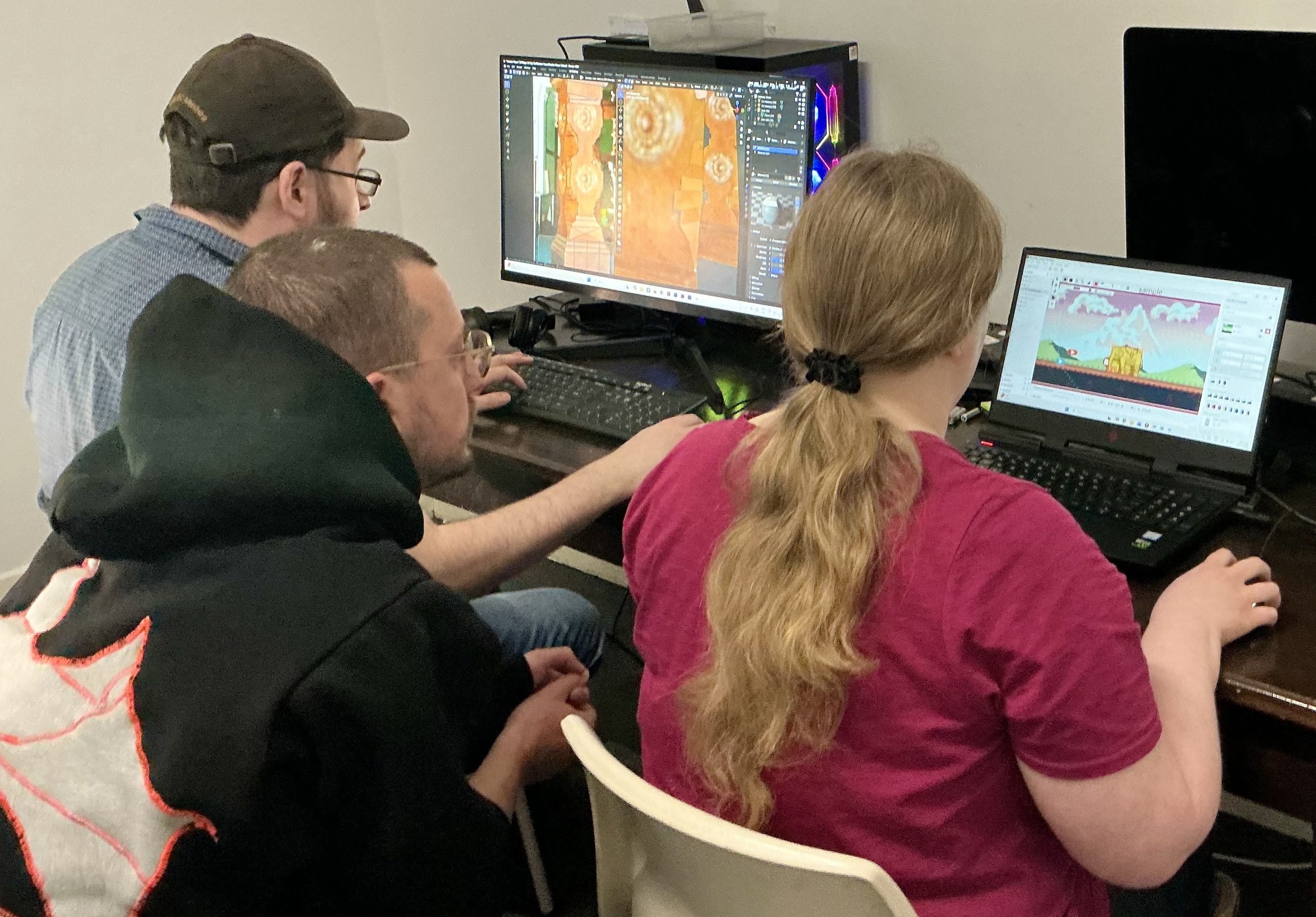 Someone supervises two people creating art on computers.