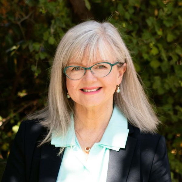 A headshot of a woman smiling, wearing glasses with long fair hair.