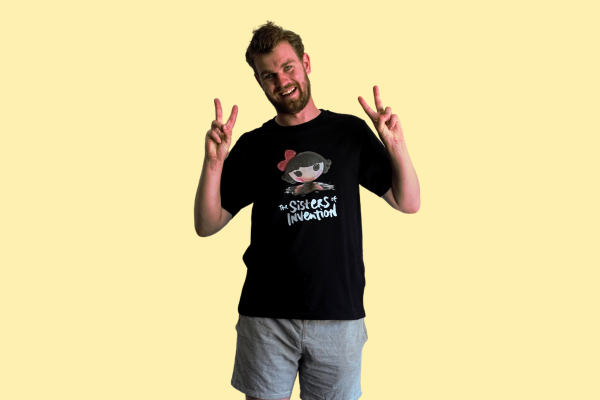 Person wearing black t-shirt with The Sisters of Invention logo featuring a doll's head in black paint.