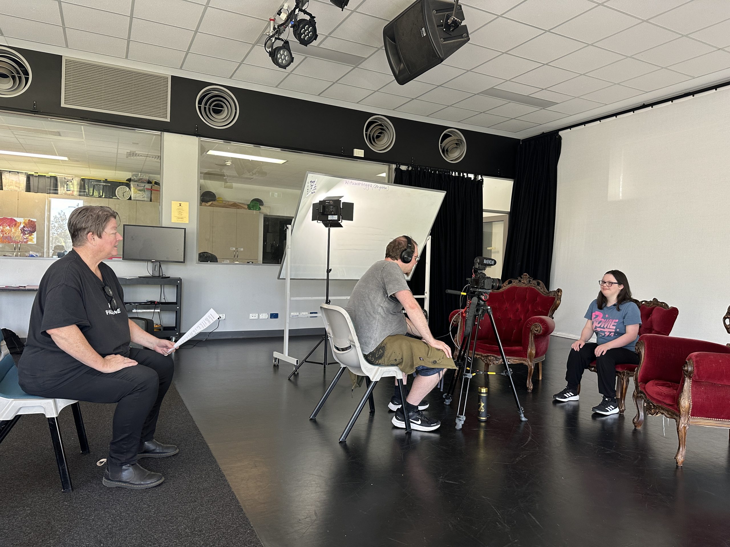 Backstage filming for Living Well videos, a member of camera crew sits in front of the actor and director. 