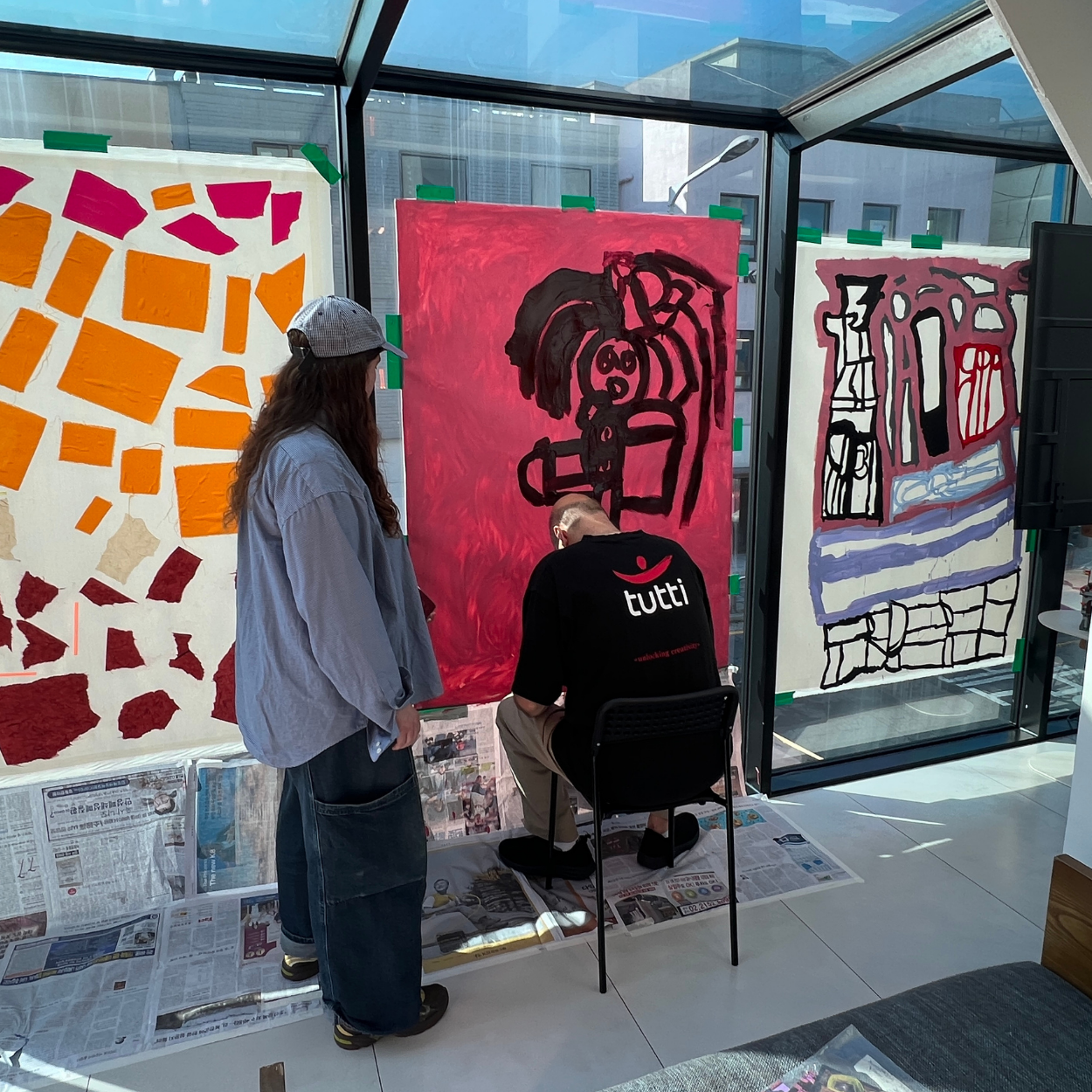 Lewis painting on a canvas taped to a window in Korea beside some previously painted works.