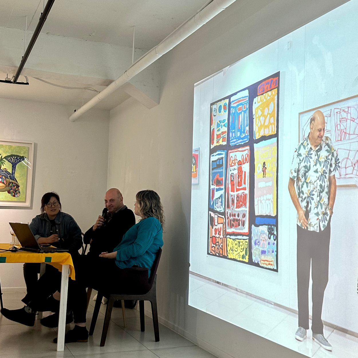 Lewis talking into a microphone as a presentation slide shows him smiling in front of one of his artworks.