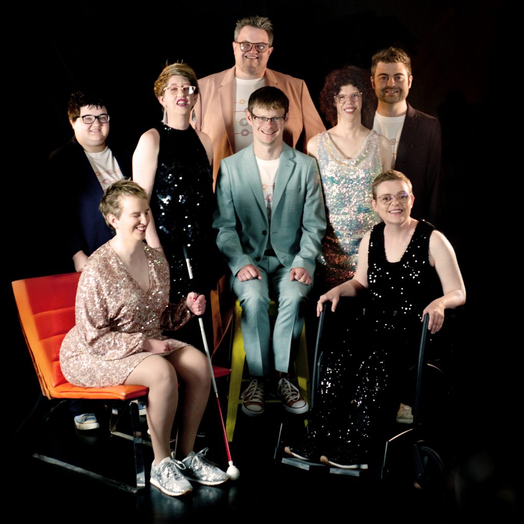 Professional photo shot of TGIF - some members standing and others sitting in a group and all smiling at the camera.