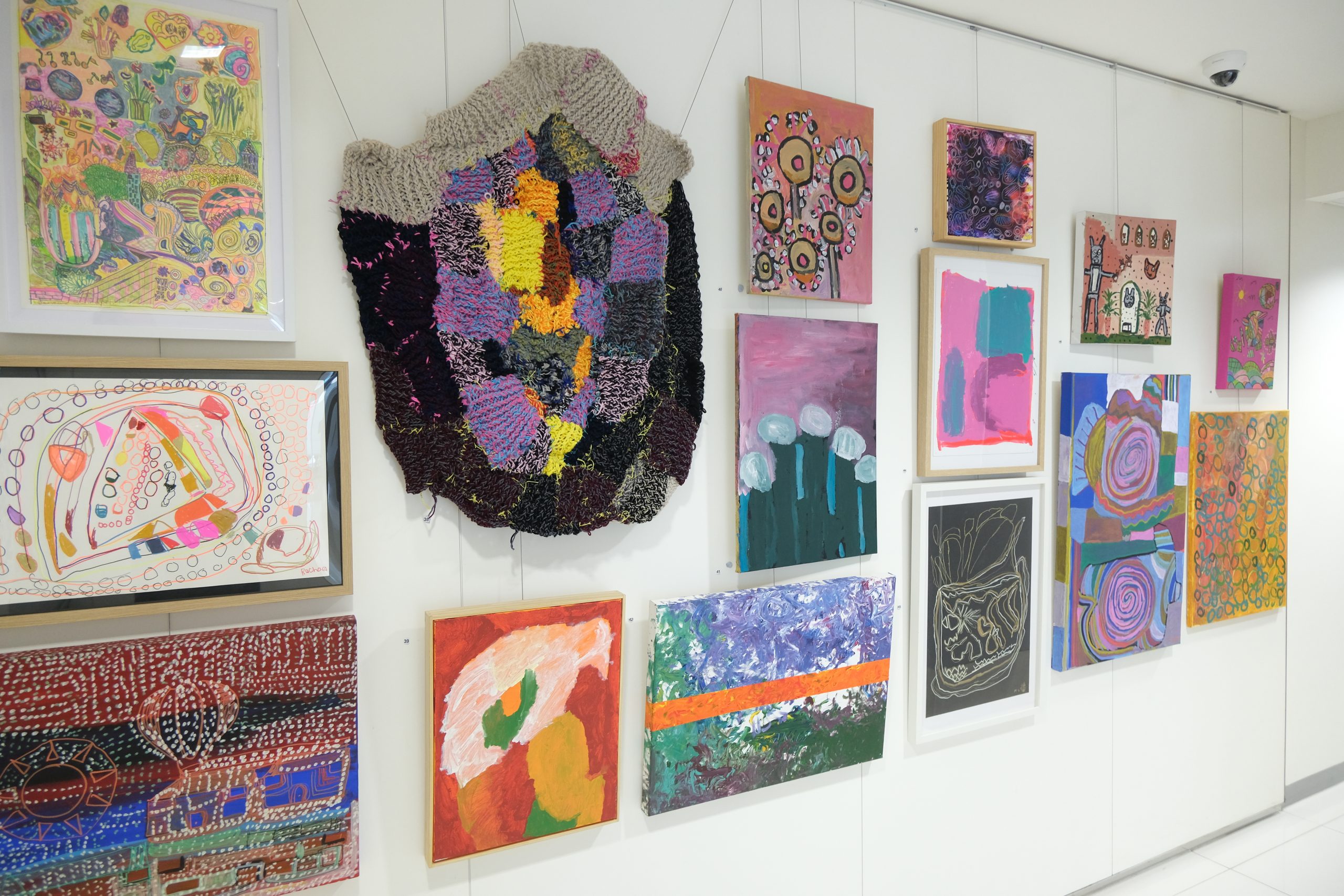 A mix of sculptural and canvas artworks hanging on a white wall. 