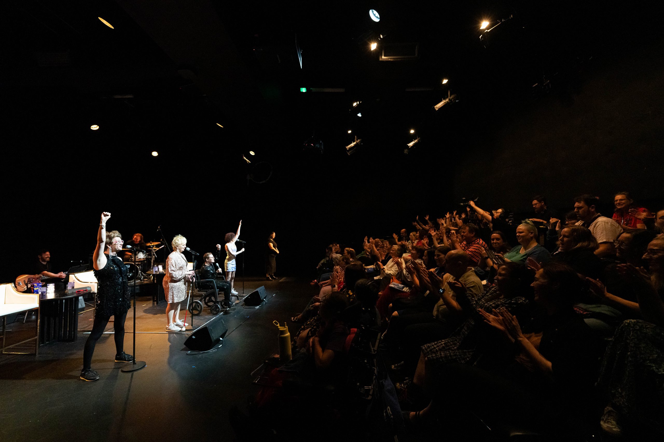 The four Sisters of Invention performing on stage in front of a full crowd of people cheering. 
