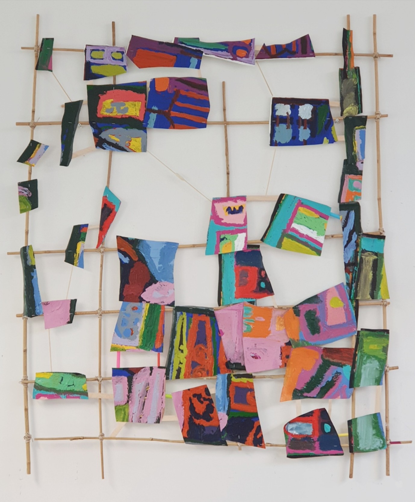 Bamboo sticks in grid with cut pieces of artwork attached. 