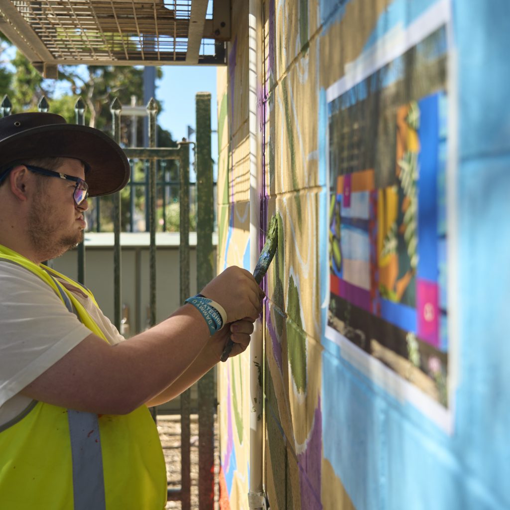Jacko Hooper painting the mural on Brighton Railway signal hut, using the digital rendering taped to the wall as a reference.