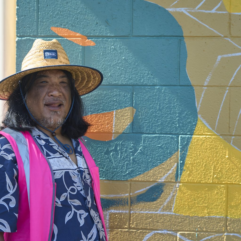 Banjobe Hunt smiling at the camera and standing by the mural work in progress.