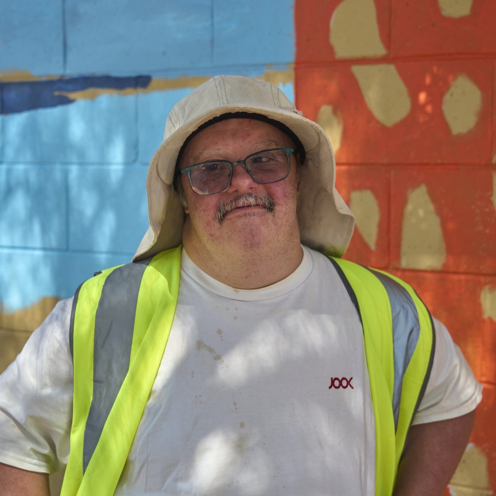 Nathan Dolphin standing by the work in progress mural and looking at the camera.
