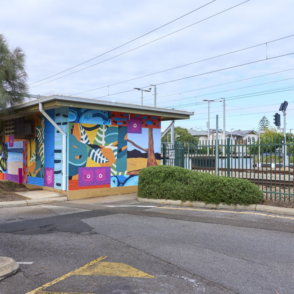 The signal hut painted with the final, bright mural. Visible are different paintings of trees and flowers in different art styles collaged together.