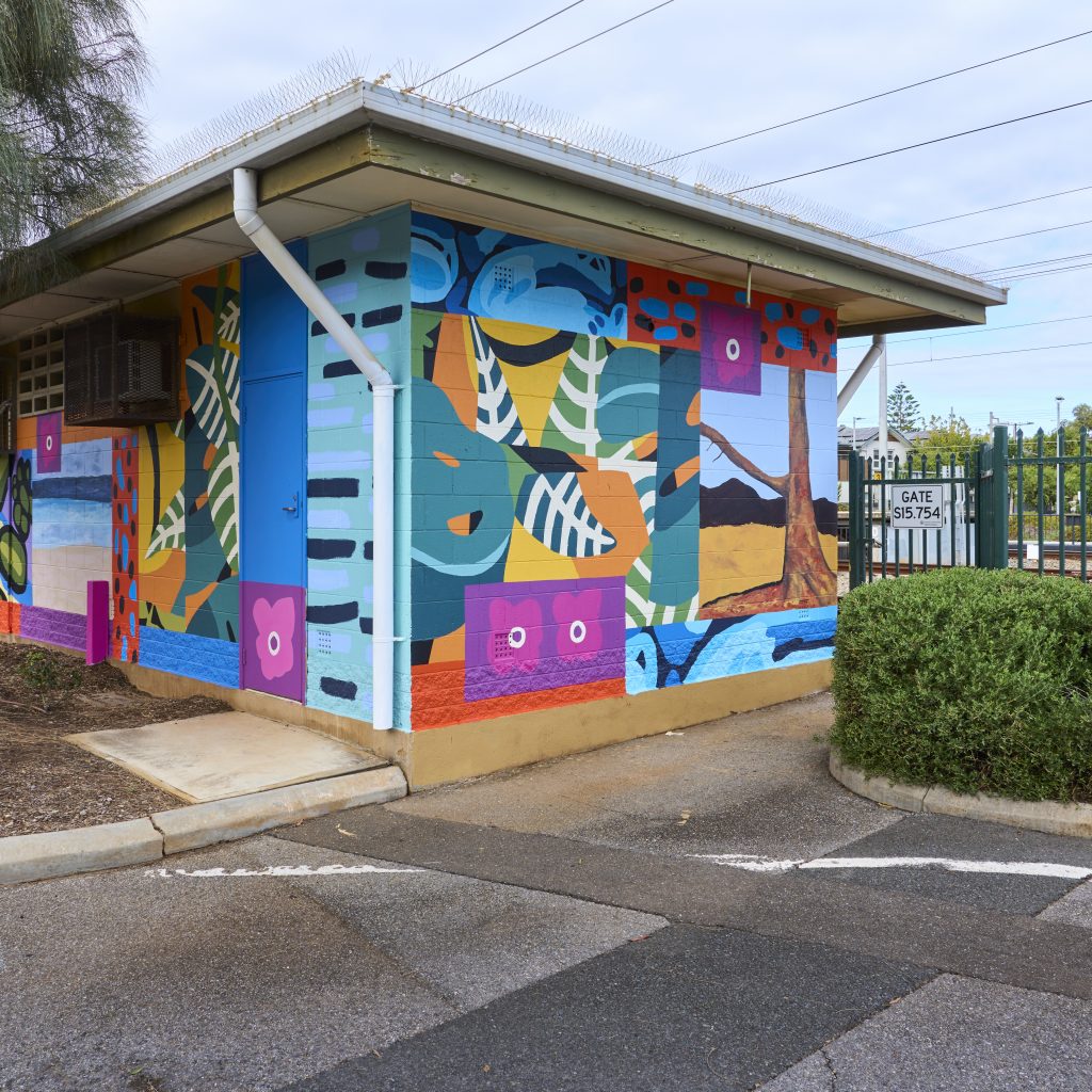 The signal hut painted with the final, bright mural. Visible are different paintings of trees and flowers in different art styles collaged together.