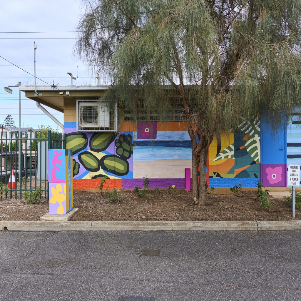 The signal hut painted with the final, bright mural. Visible are different paintings of trees and flowers in different art styles collaged together.