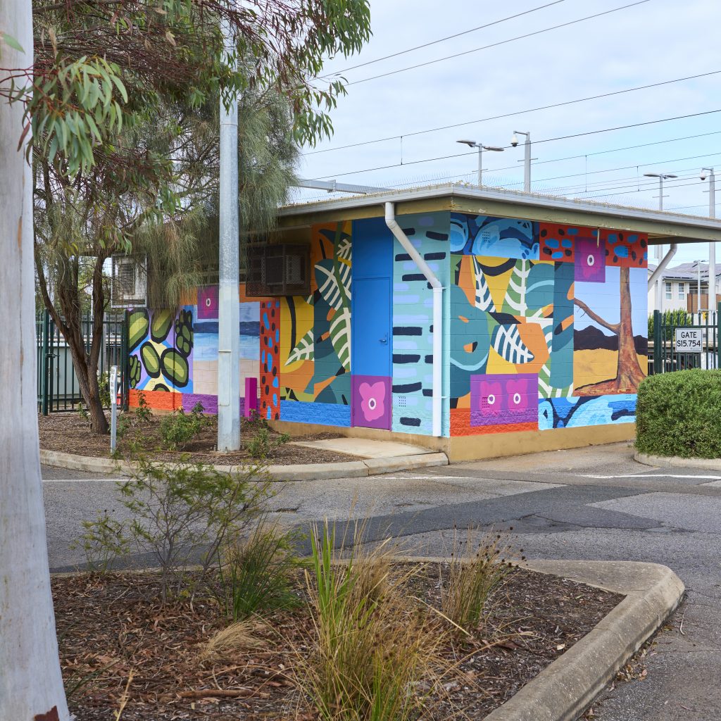 The signal hut painted with the final, bright mural. Visible are different paintings of trees and flowers in different art styles collaged together.