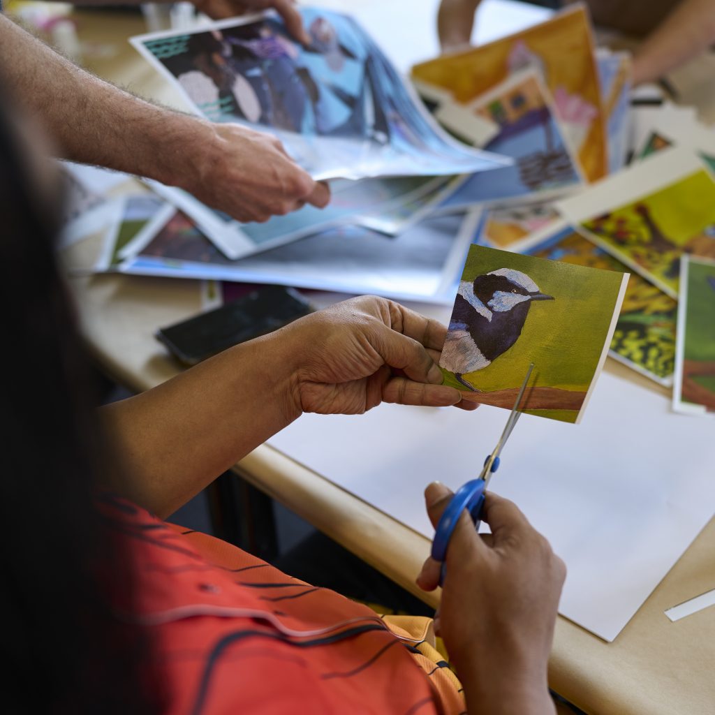 Person cutting up a print out of an artwork showing a hyper realistic bird.