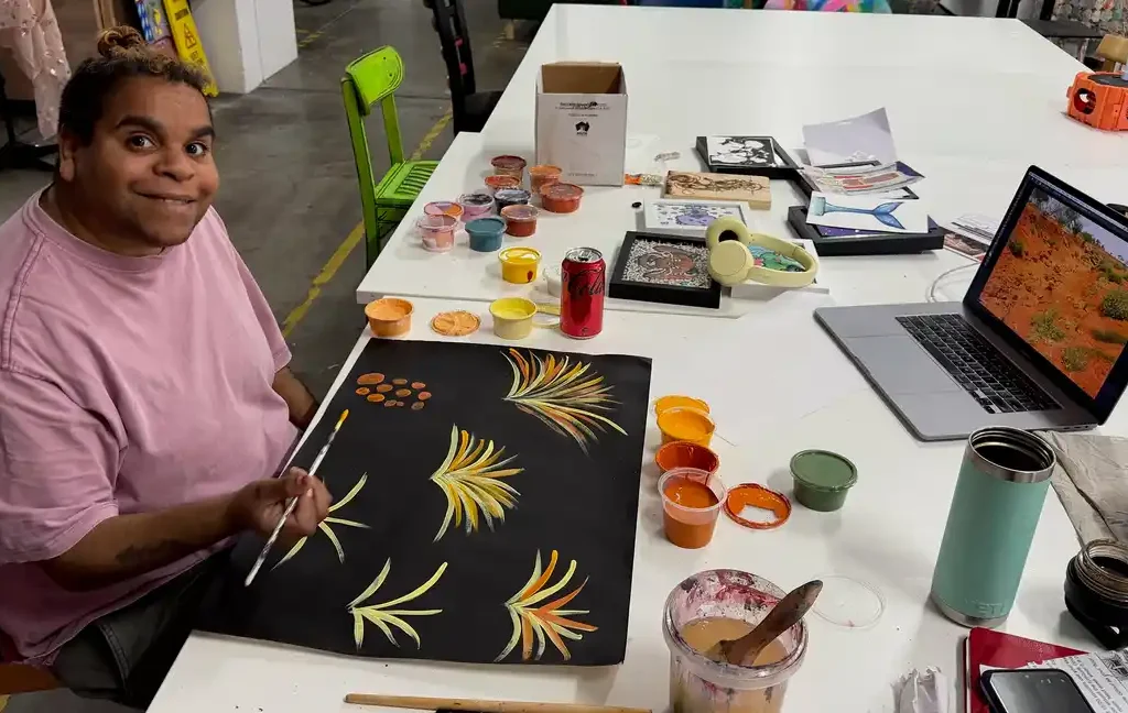 Tutti Artist Jackie Saunders sits a table surrounded by painting materials, while working on some art for Silent Country Exhibition