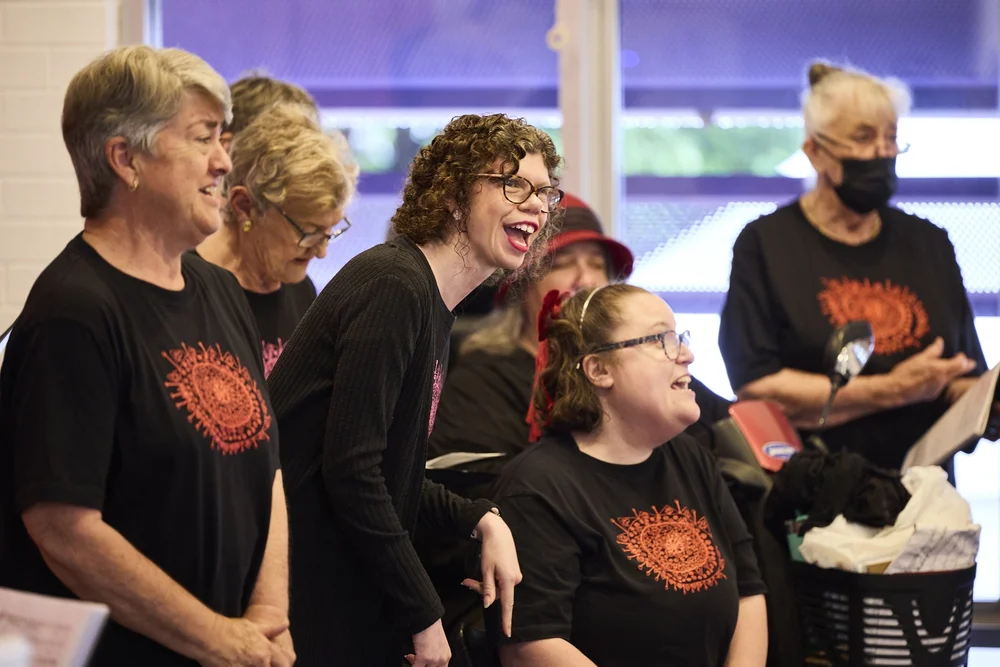 A group of people stand together smiling and singing.